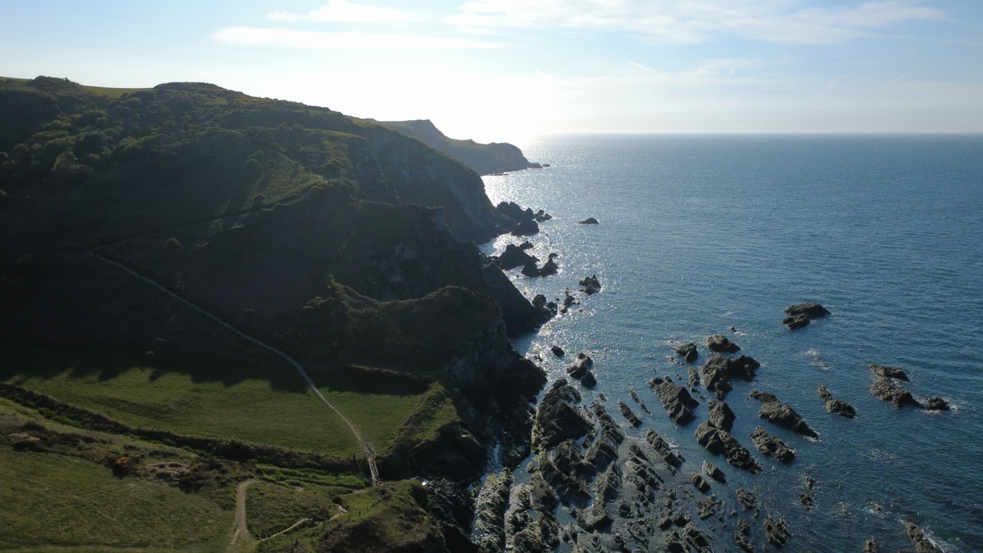 A cliffside Devon coastal path above the sea in bright afternoon light