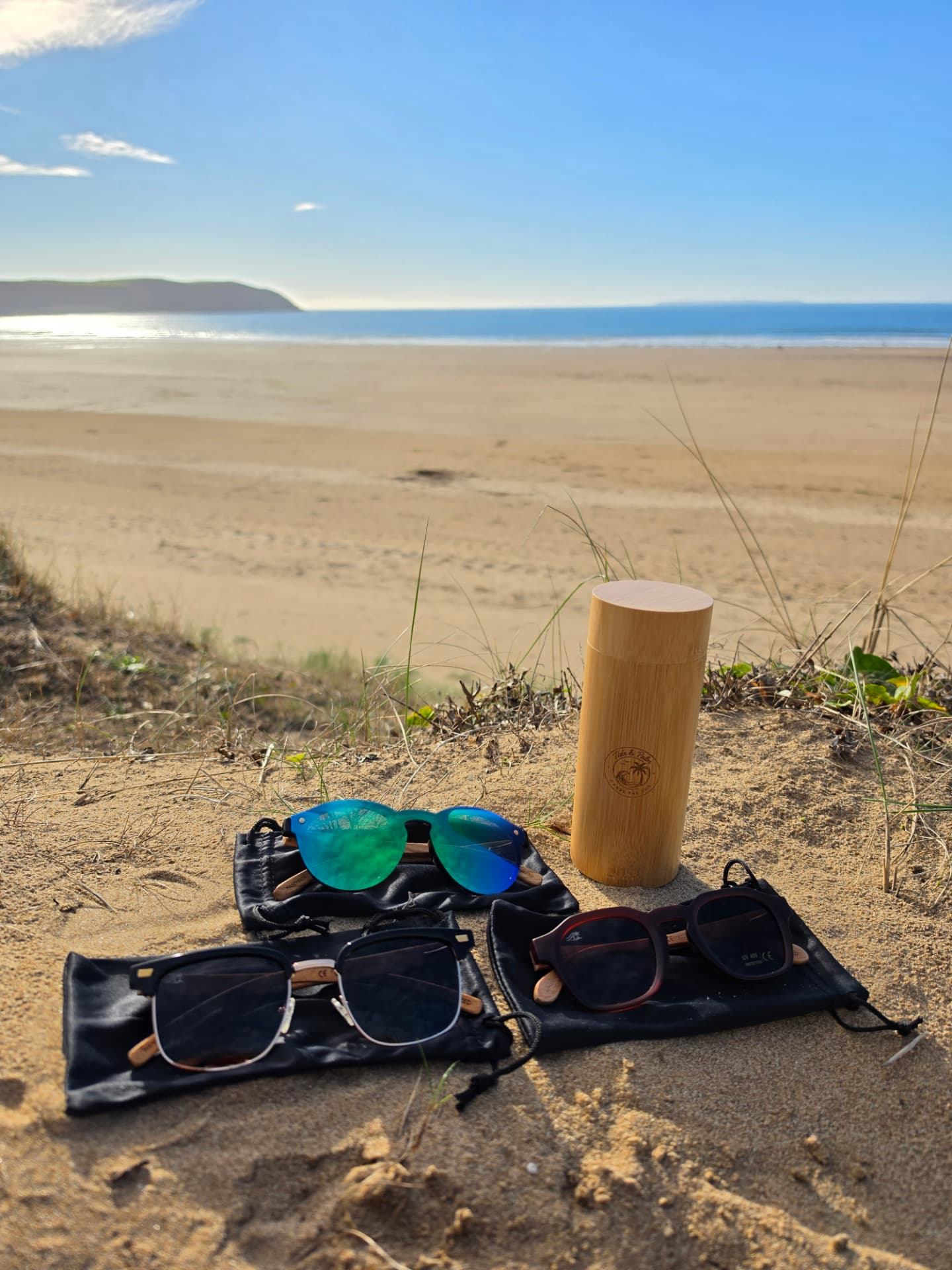 Three pairs of Tide & Palm sunglasses with the bamboo case on the dunes above the beach